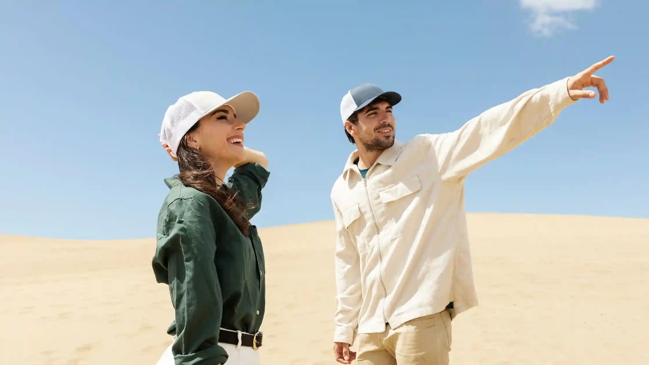 Couple exploring the desert dunes during an Abu Dhabi layover, pointing toward the horizon under a clear blue sky.